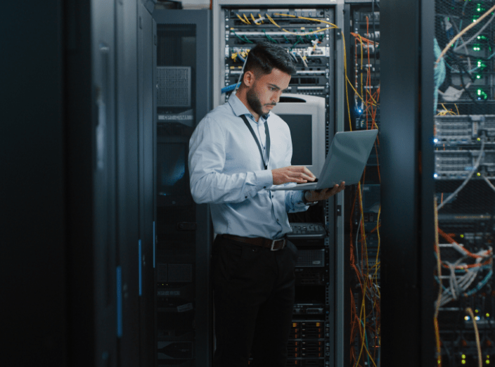 A man holding a laptop near IT servers.