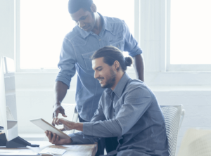 A pair of coworkers looking at a notebook and talking to each other.