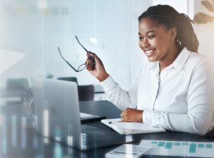 A woman smiling at a laptop screen.
