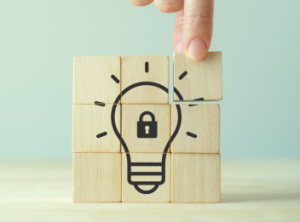 A hand using building blocks to make a lightbulb with a padlock in the middle.