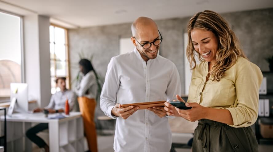 Two coworkers looking at an iPad and a phone screen.