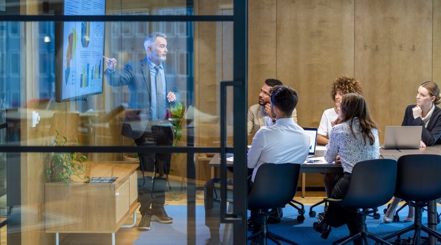 A meeting in a boardroom with team members looking at graphs on a screen.