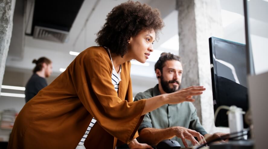 A person looking at a coworkers screen and discussing it.