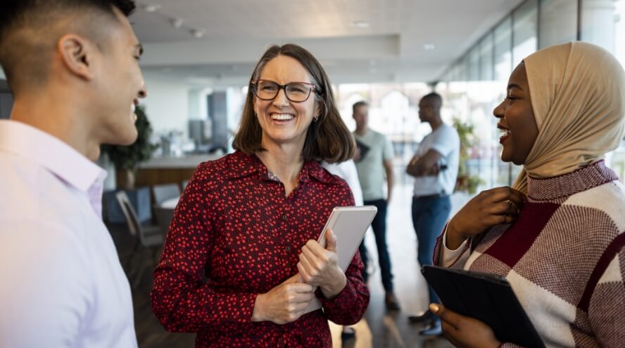 Three coworkers standing and laughing in a casual office setting.