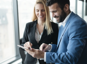 Two colleagues dressed in business attire are looking at an iPad screen.