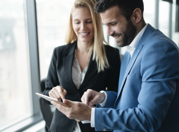 Two colleagues dressed in business attire are looking at an iPad screen.