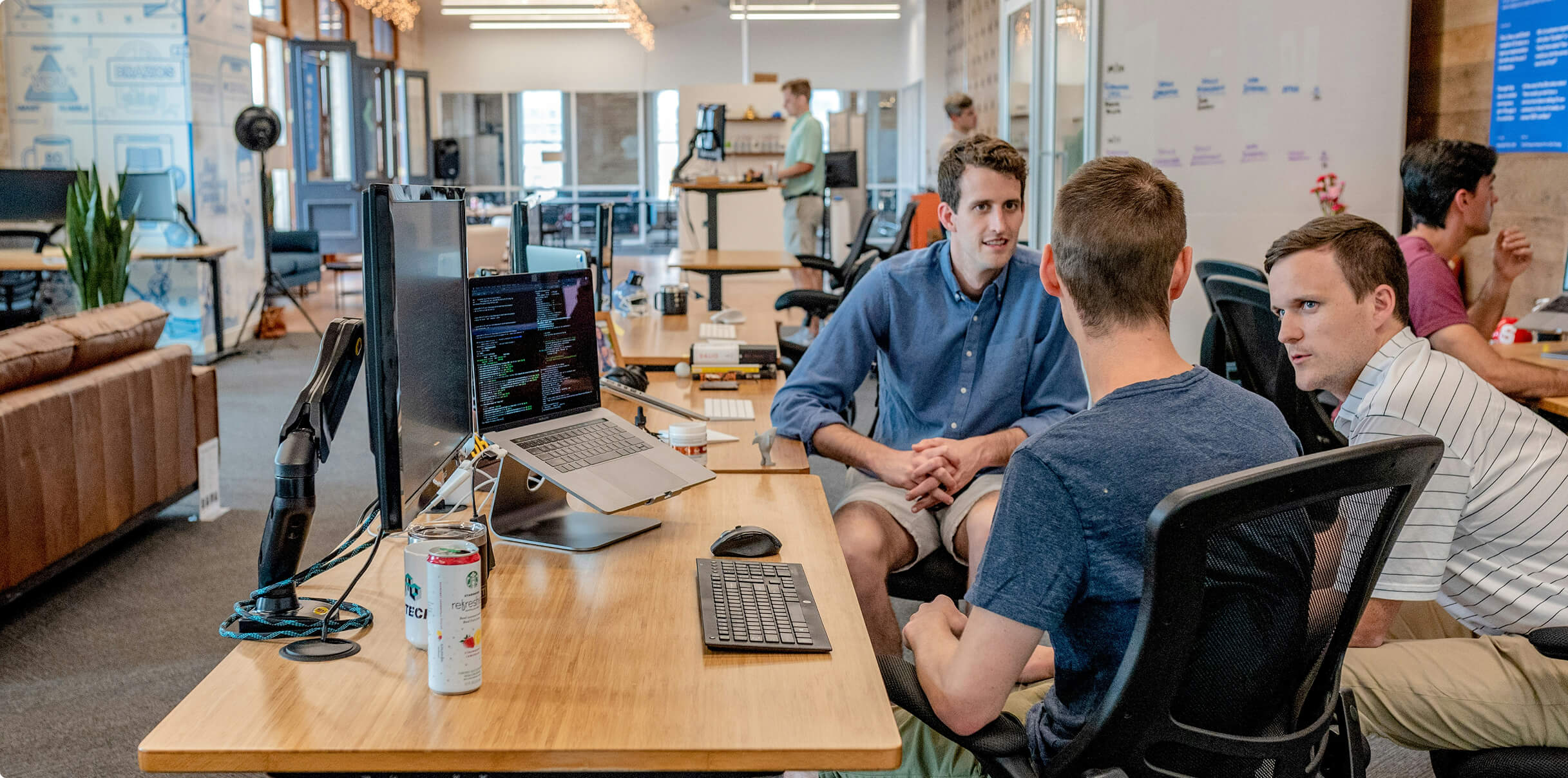 Three coworkers gathered around a desk in discussion.