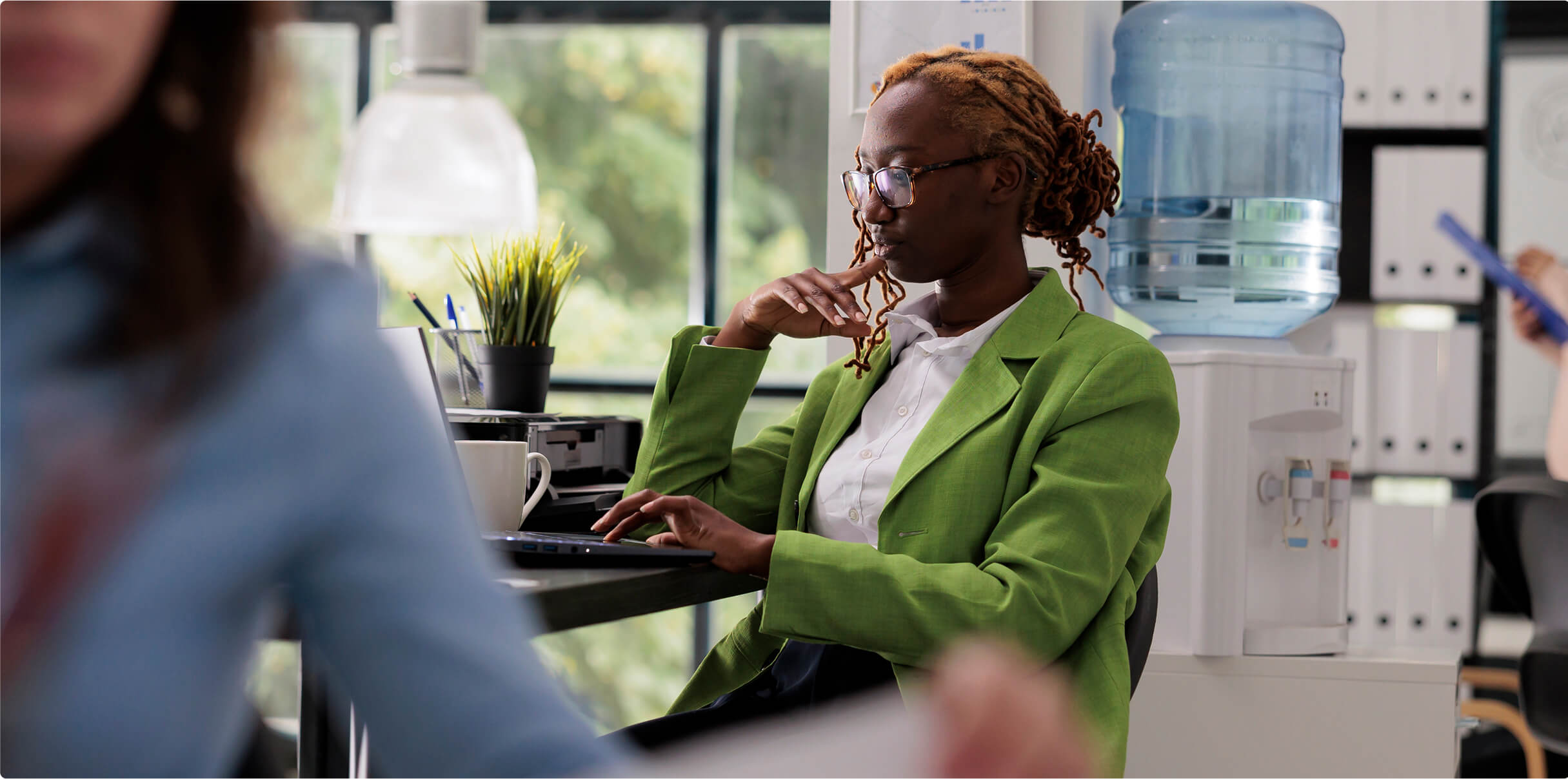 A woman in a bright green blazer sitting deep in thought in front of a laptop screen.