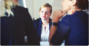 A woman looking ahead while sitting at a boardroom table.
