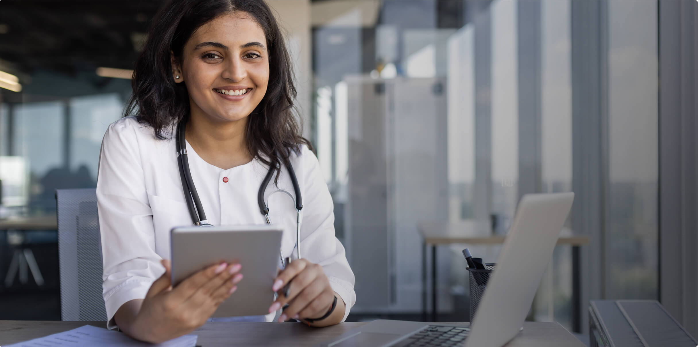 A woman wearing a stethoscope and holding an iPad.