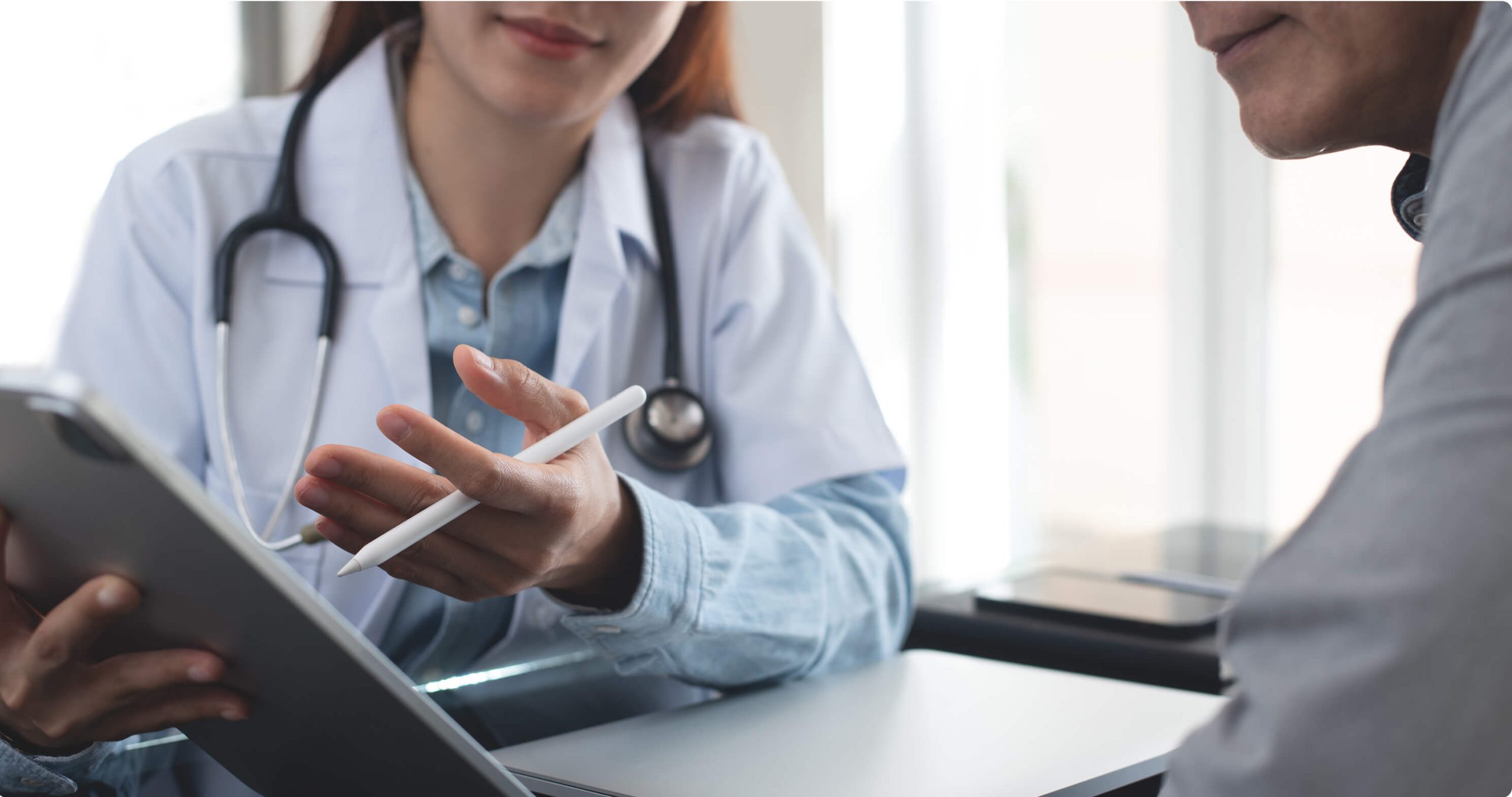 Close up of a healthcare professional wearing a stethoscope and discussing something on an iPad screen with a patient.