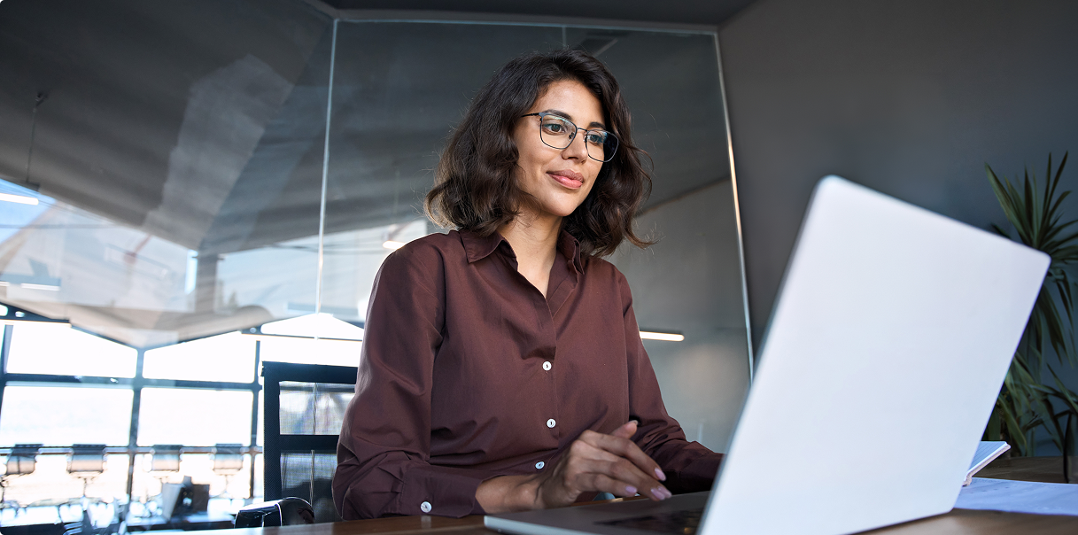 Woman wearing a burgundy shirt and glasses sitting with a laptop.