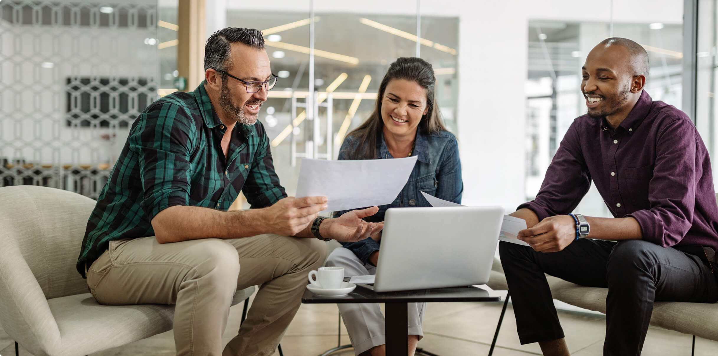 Three coworkers gathered for coffee while discussing papers.