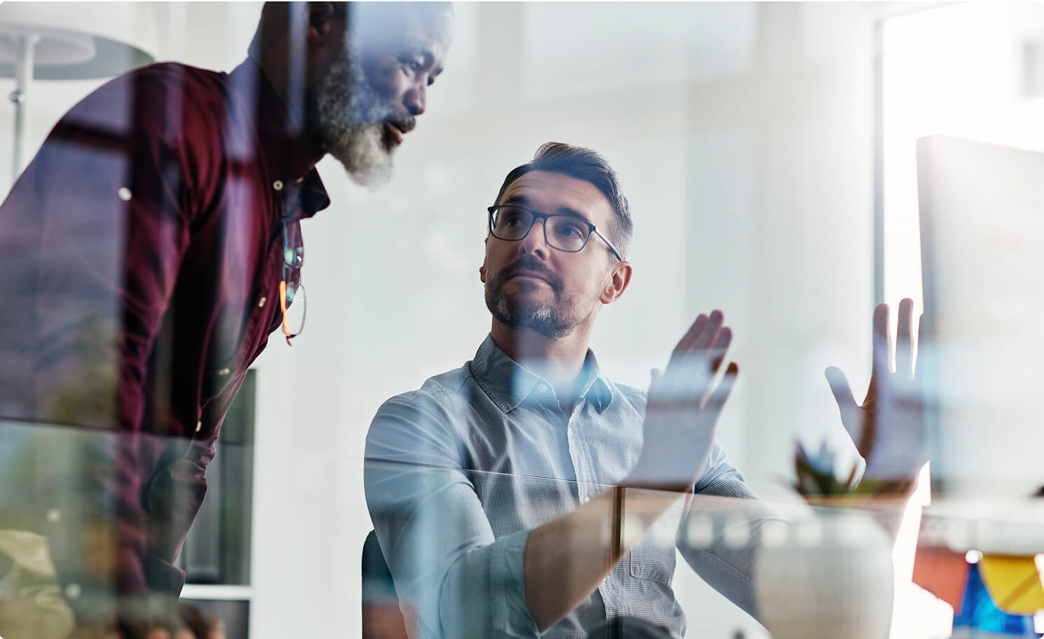 An office worker explaining a concept to an onlooking coworker, using hand gestures.