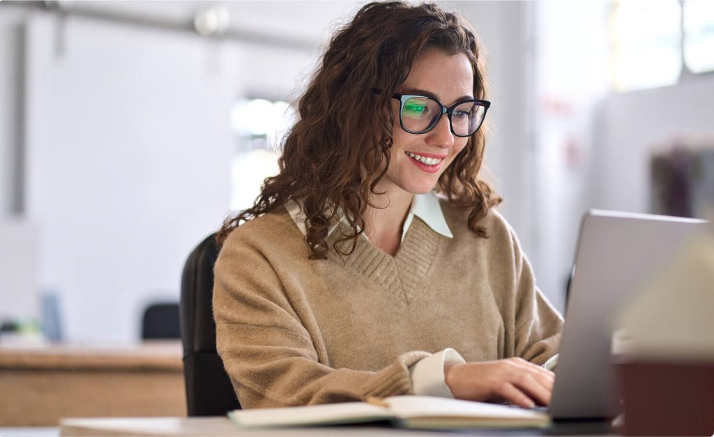 A person sitting at a laptop and smiling down at the screen.