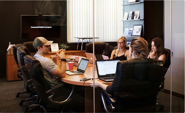 A group of coworkers sitting and discussing something in a glass boardroom.