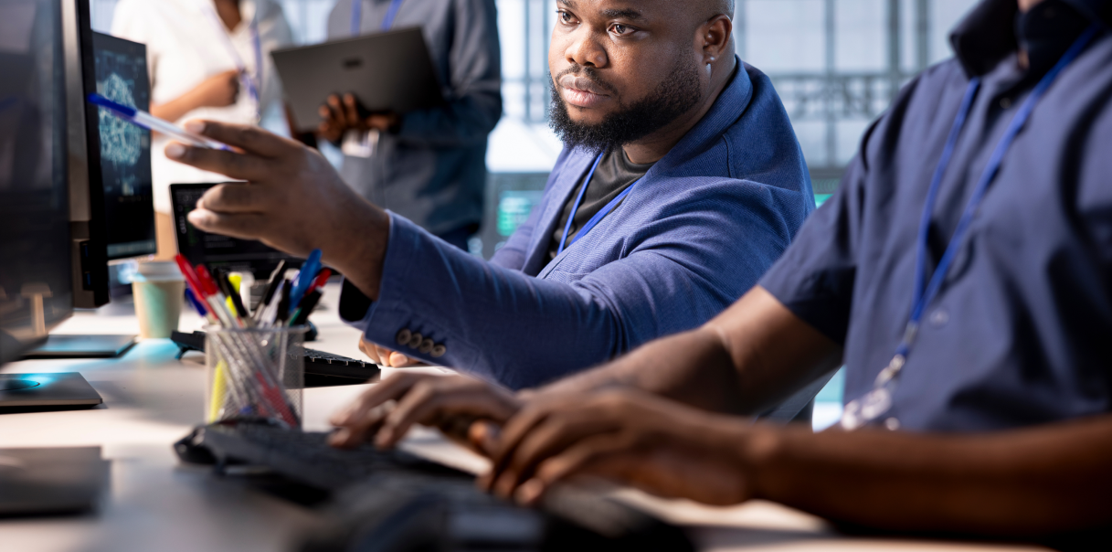 A man pointing to a coworkers monitor.
