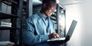 A man smiling, holding a laptop in one hand and scrolling on the control bar with the other.