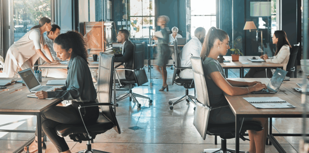 An open office concept with people sitting at desks and working on laptops.