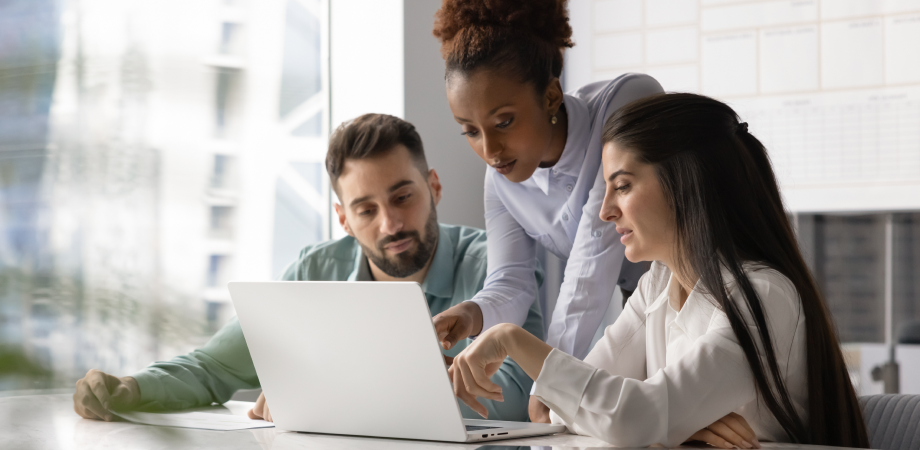 Three colleagues surrounding a laptop in deep discussion.