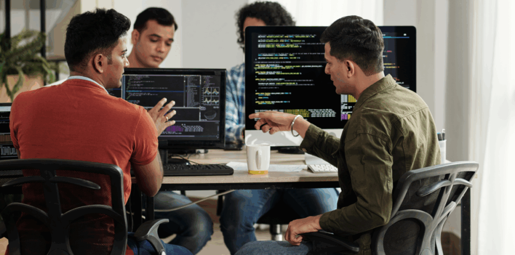 Two coworkers looking at monitors with code on screen.