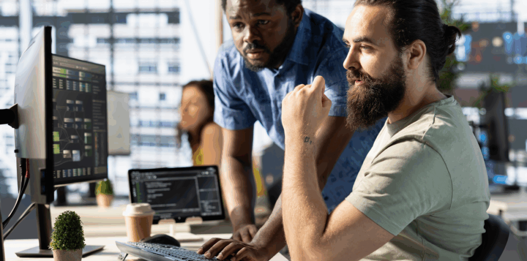 Two coworkers at a desk, looking at a dual-monitor set up.