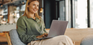 A woman sitting down on a chair and typing on a laptop.
