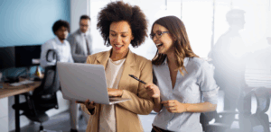 Two coworkers looking at a laptop screen and smiling.