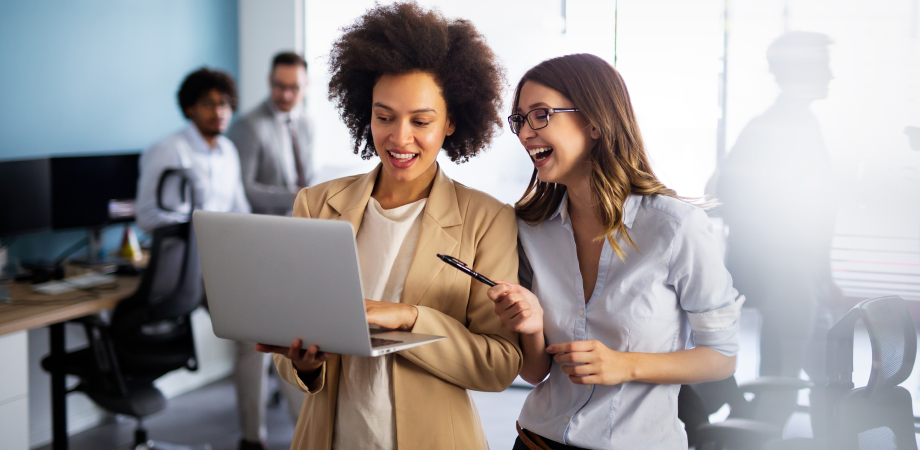 Two coworkers looking at a laptop screen and smiling.