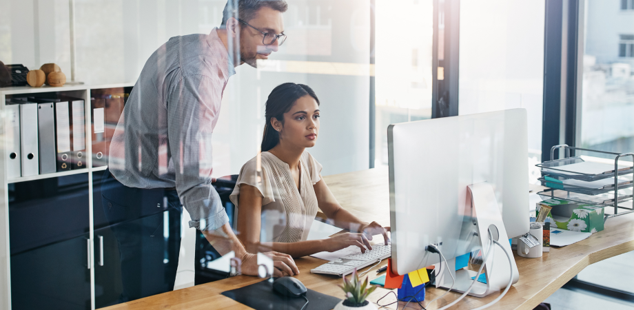 Two coworkers at a desk looking at a computer screen.