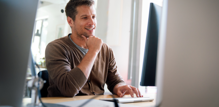 A man sitting in front of a computer monitor in a thoughtful pose.
