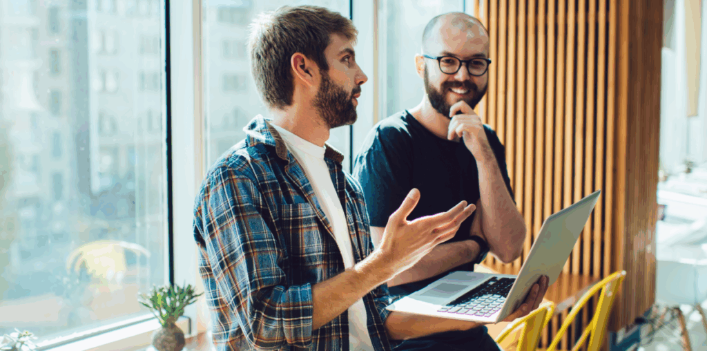 Two coworkers are discussing an idea in front of a laptop.