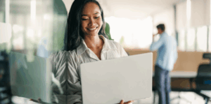 Woman sitting at a desk and holding a laptop in her hands.