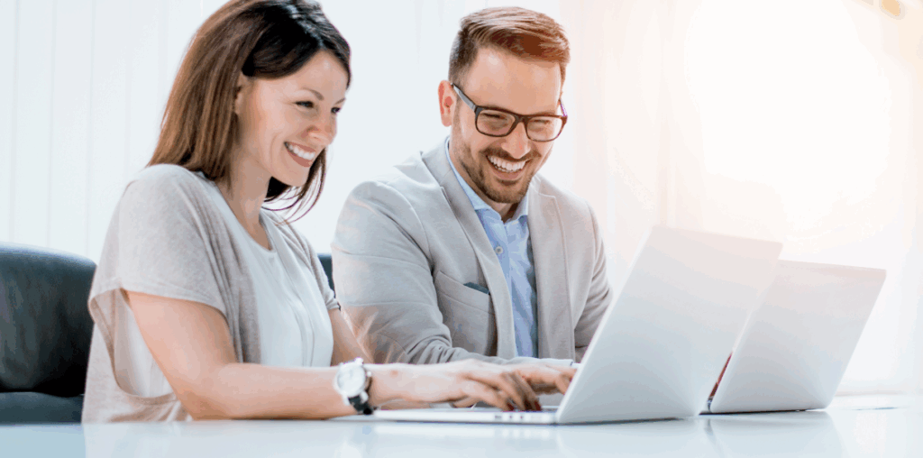 Two coworkers sitting beside each other and looking at a laptop screen.