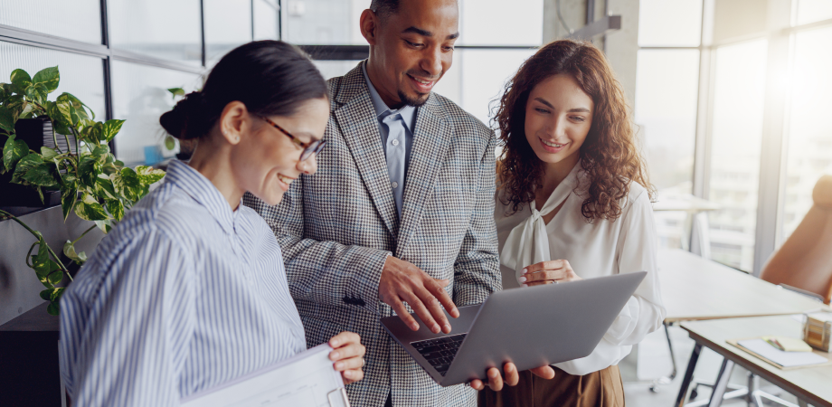 Three coworkers standing together looking at something on a laptop screen.