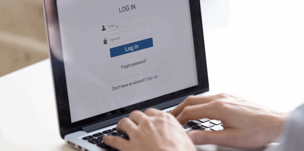 Two hands actively typing on a keyboard. The laptop screen shows a login prompt.