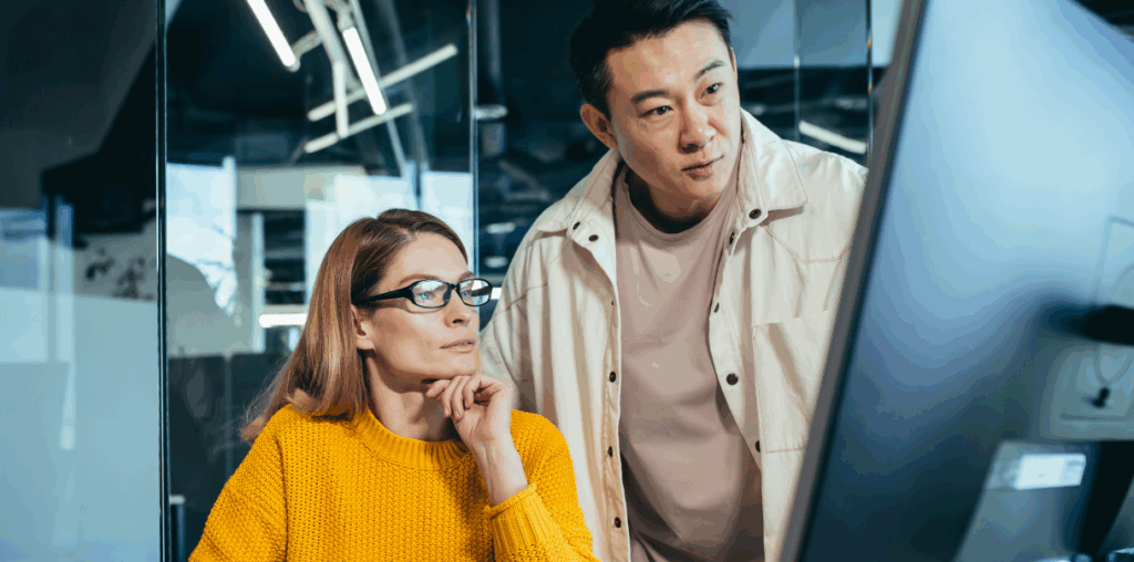 Two coworkers looking deep in thought at a computer screen.