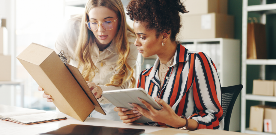 Two coworkers looking at an iPad and a cardboard shipping box.