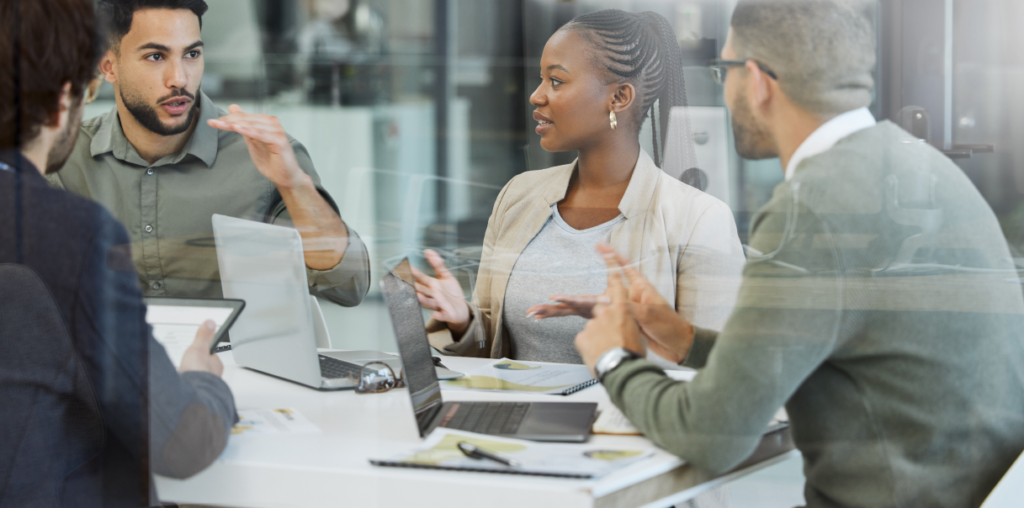 A team discussing a project at a table. Each have their laptop open.